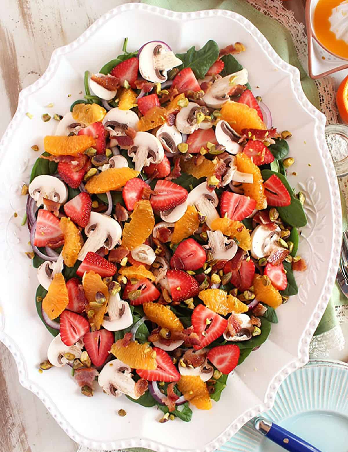 Overhead shot of strawberry spinach salad with oranges on a white oval platter.