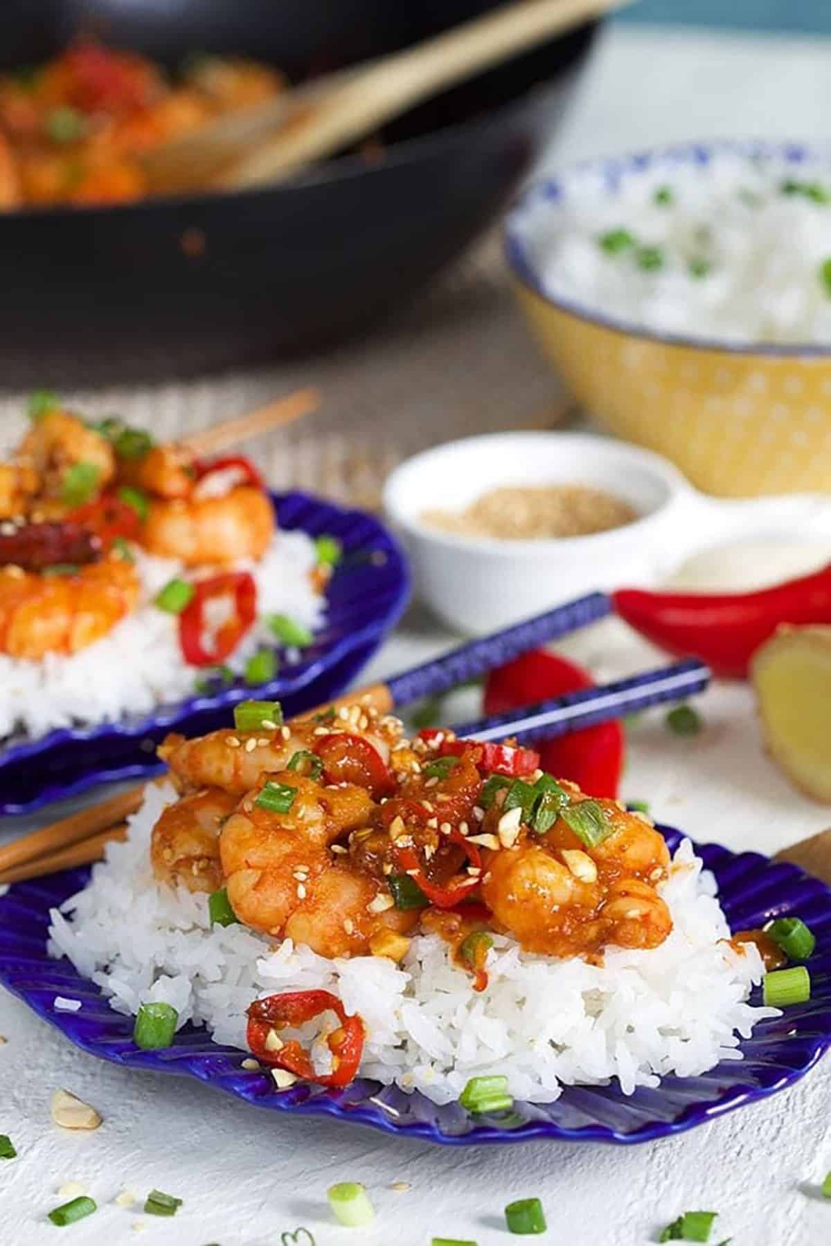 Easy Szechuan Shrimp recipe on a bed of white rice on a square blue and white plate with silver chopsticks.