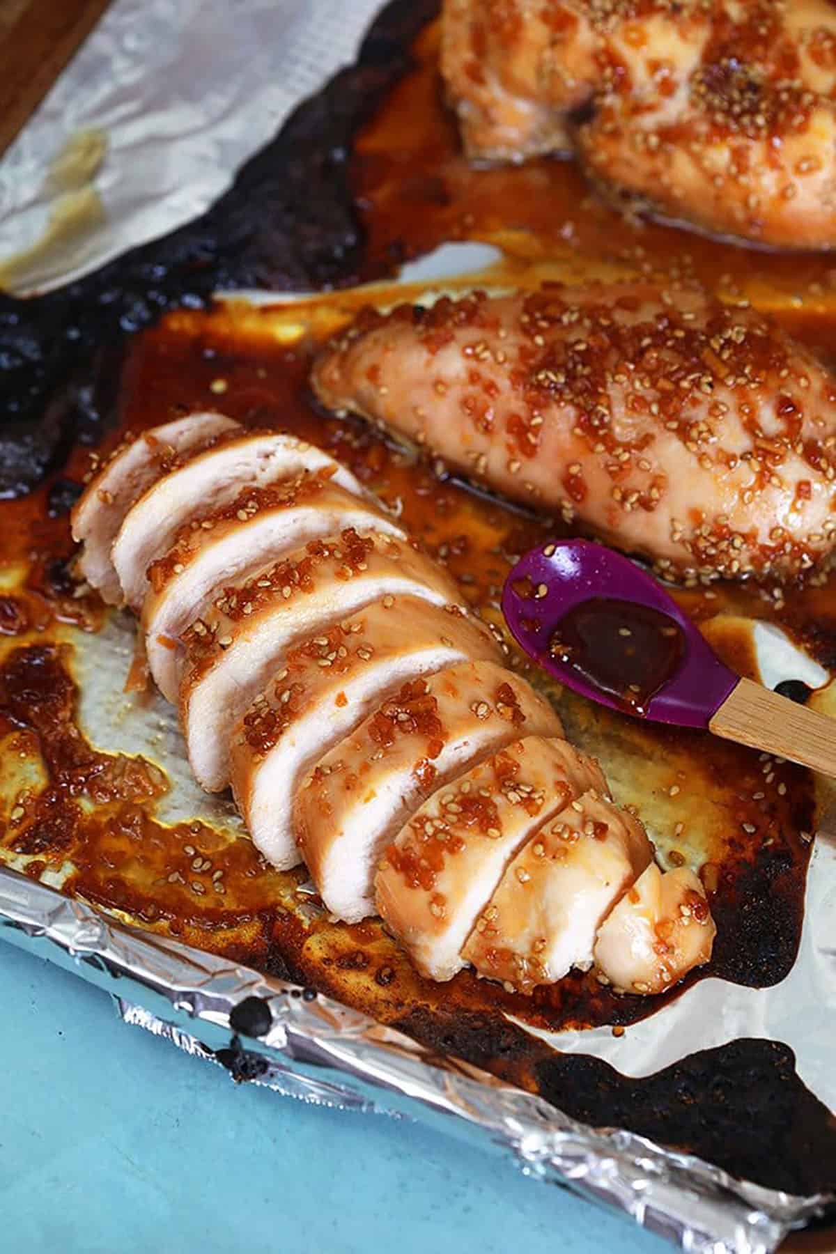 Sliced baked teriyaki chicken breast on a baking sheet lined with foil.