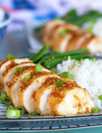 Sliced teriyaki chicken breast on a plate with rice.
