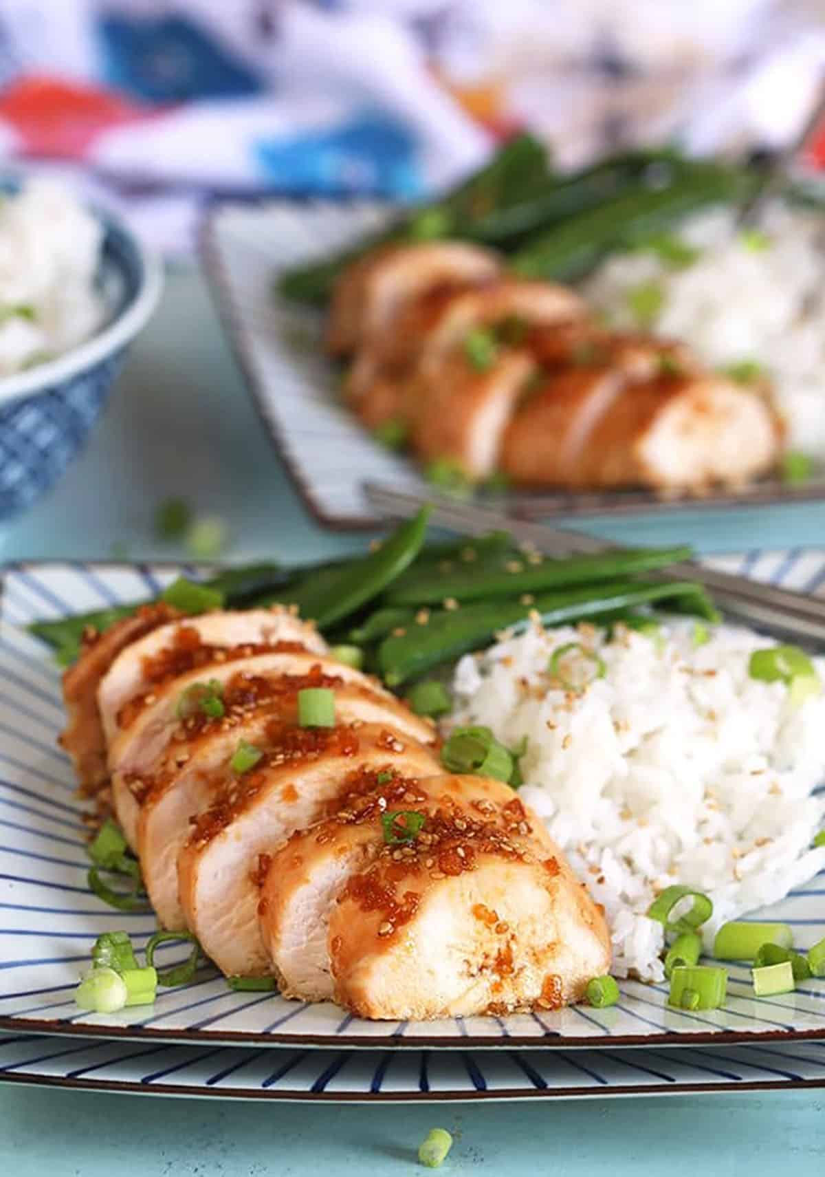 Sliced Teriyaki Chicken breast on a plate with rice and green beans.