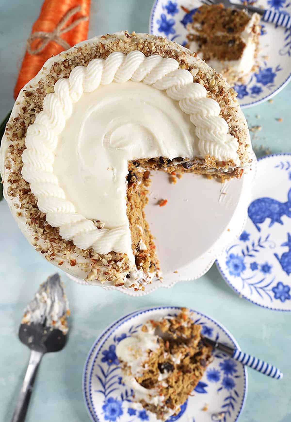 overhead shot of carrot cake on a cake plate with a slice on a blue and white plate.