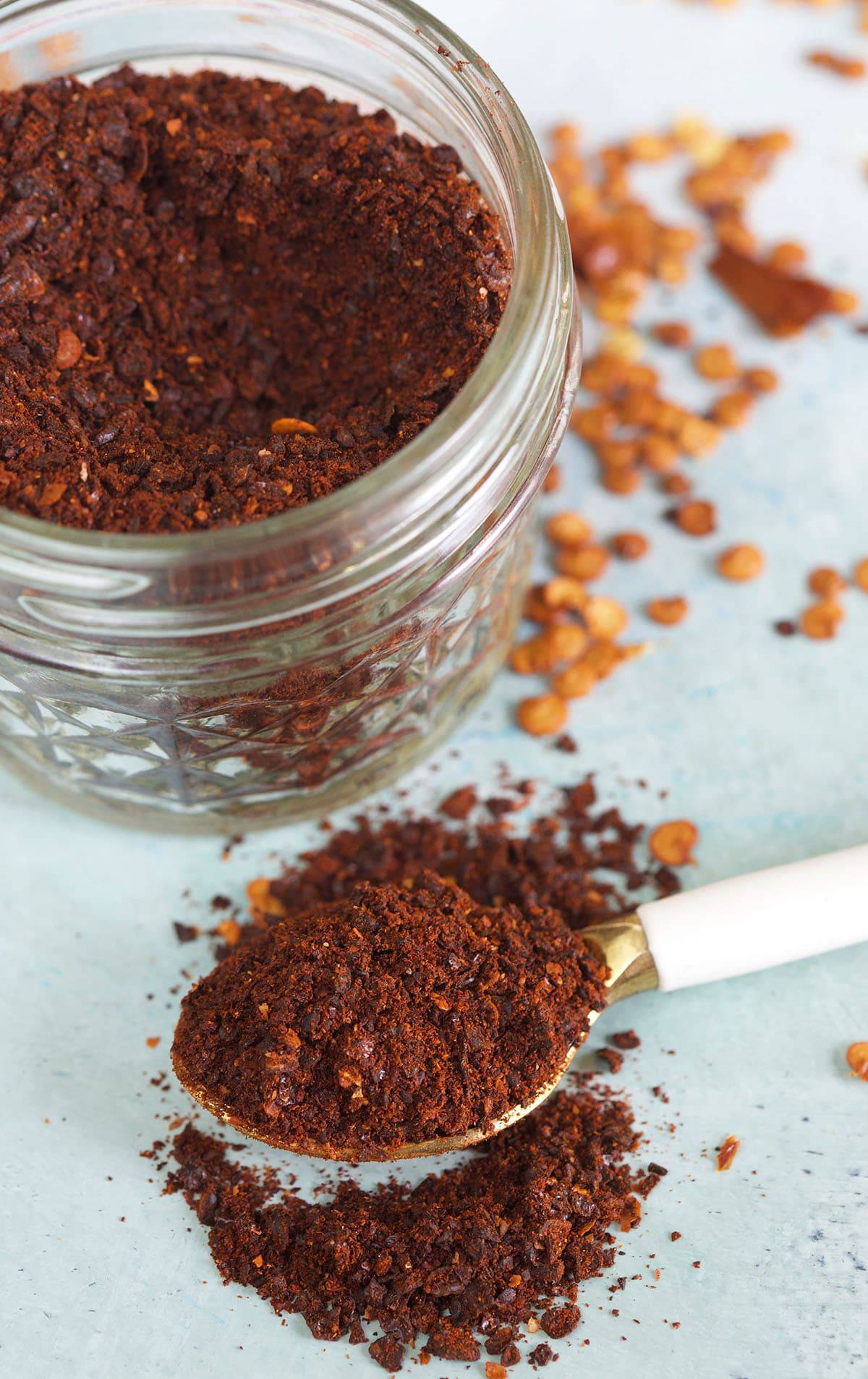 A spoon full of chili powder is placed next to a full jar.