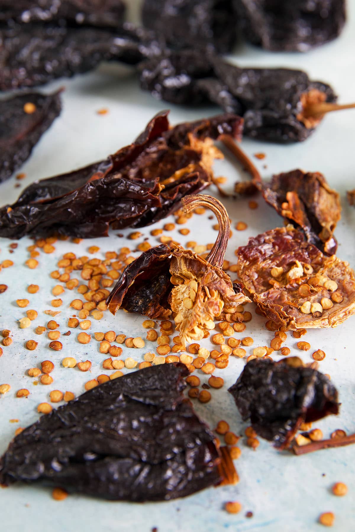 Ancho chilis are broken on a white surface, revealing many seeds.