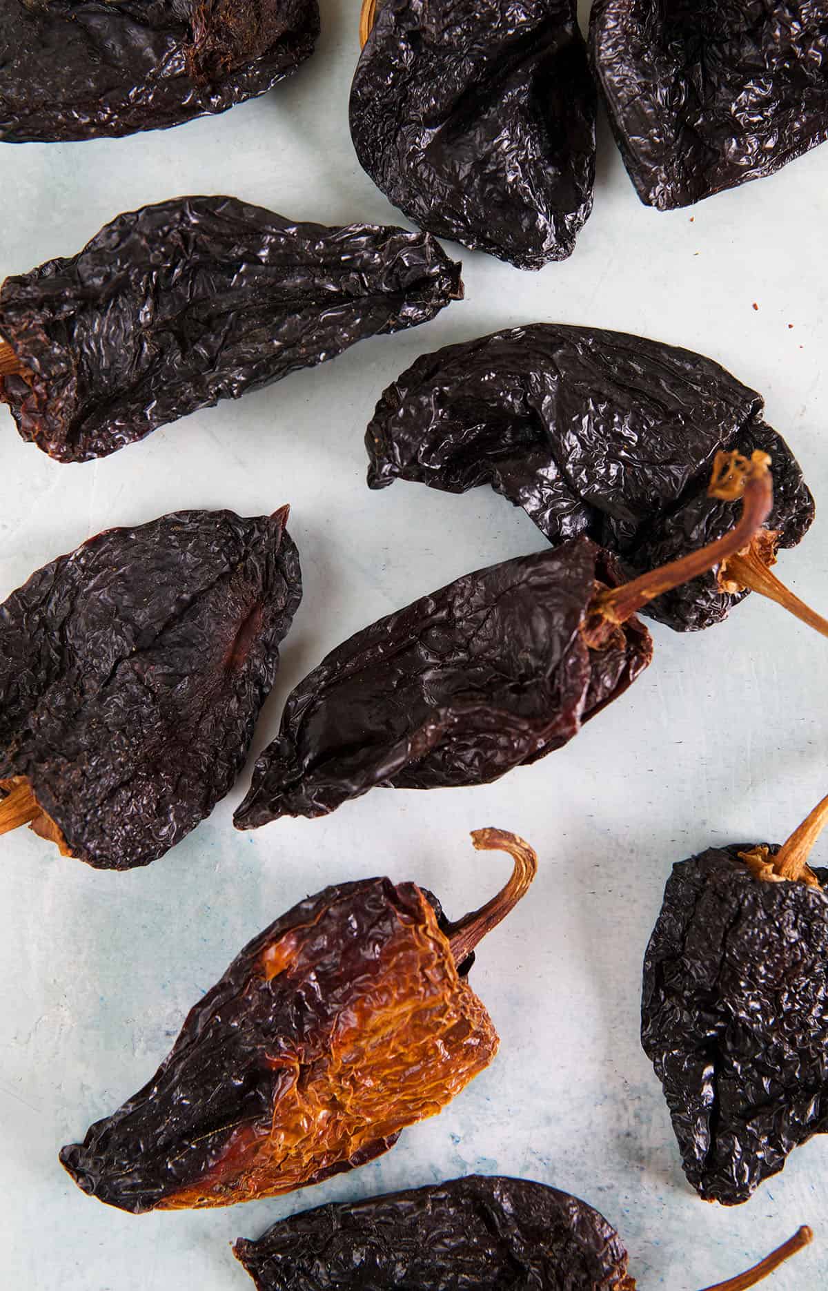Dried whole ancho chilis are placed on a white surface.