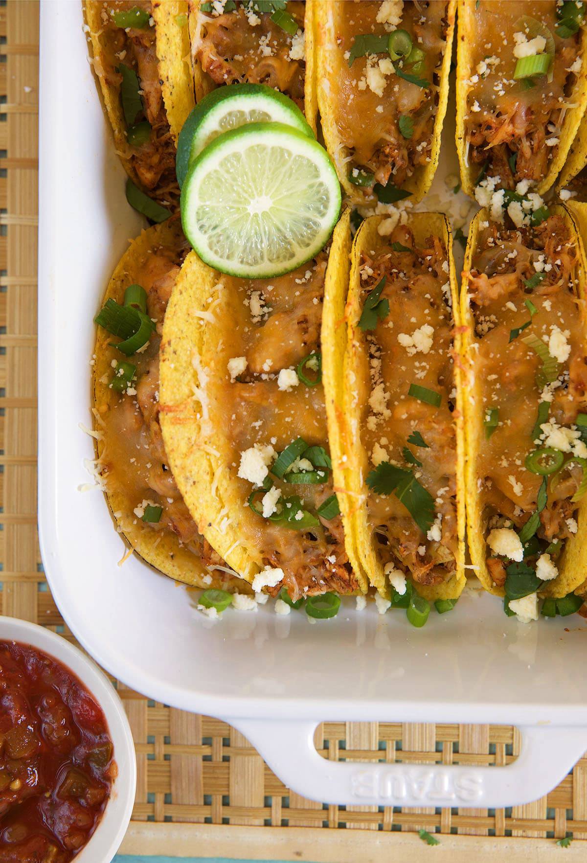 Chicken tacos are lined up and filling a white casserole dish.