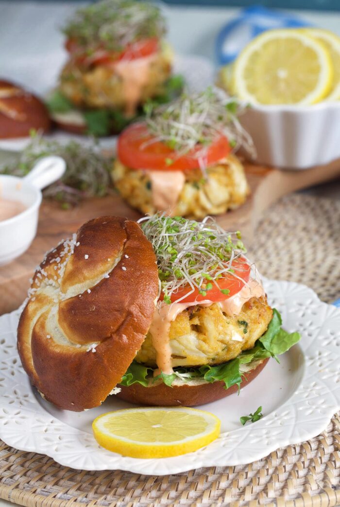 A pretzel bun is placed beside a crab cake sandwich.
