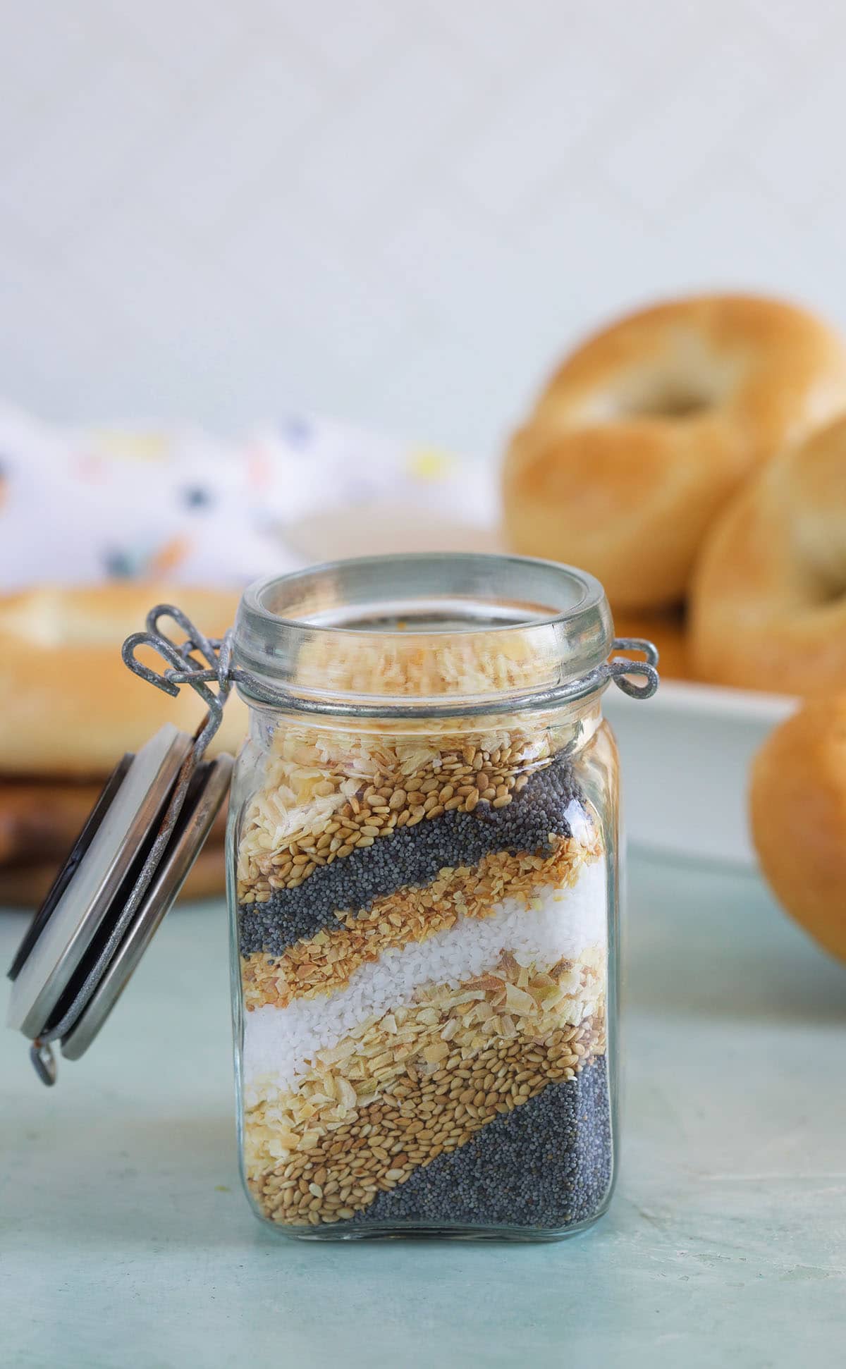 layered everything bagel seasoning ingredients in a small jar on a blue background.
