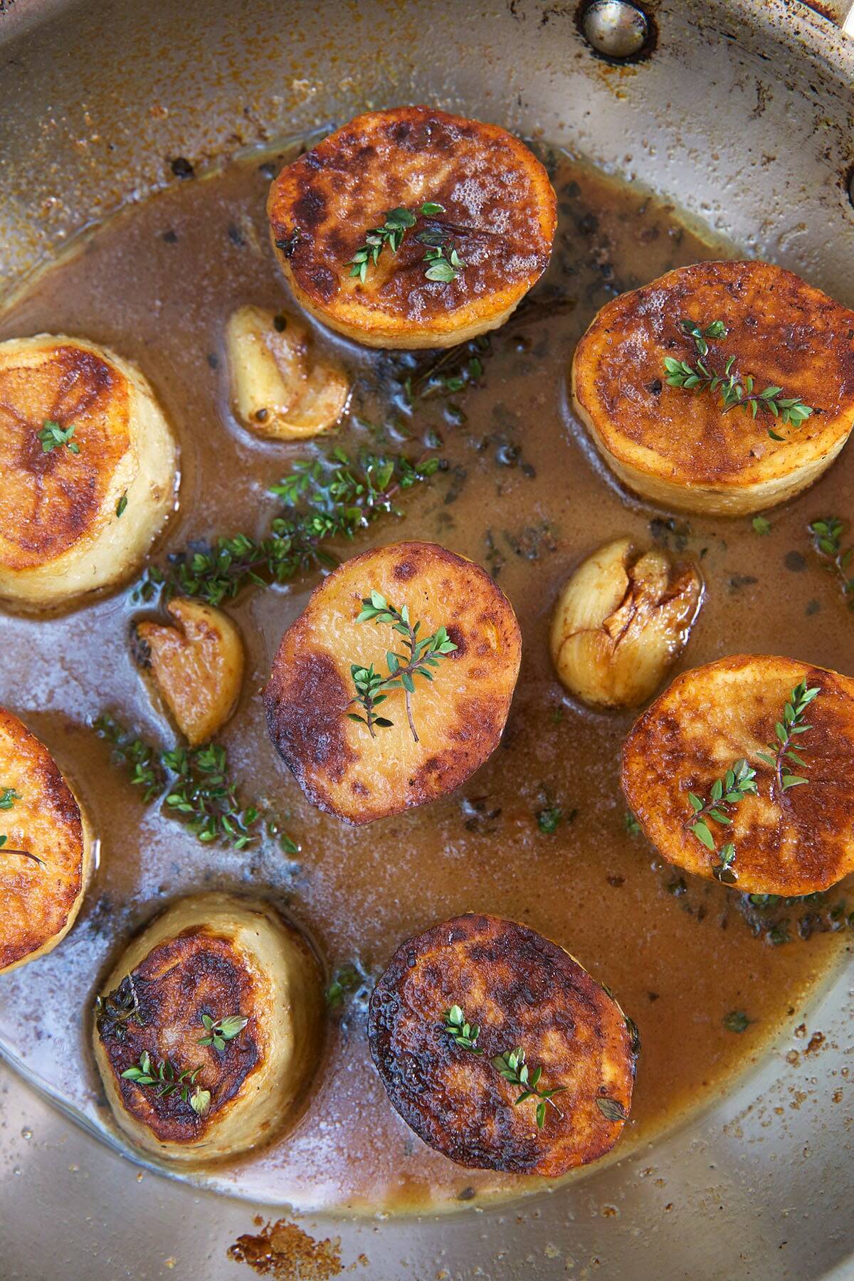 Garlic cloves are placed in between potatoes in a skillet.