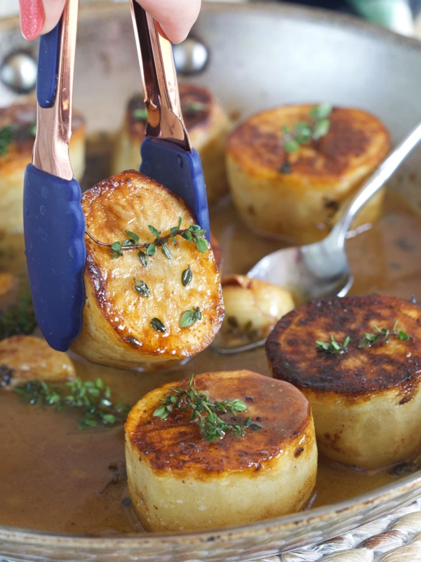 A potato is being lifted from the skillet with tongs.