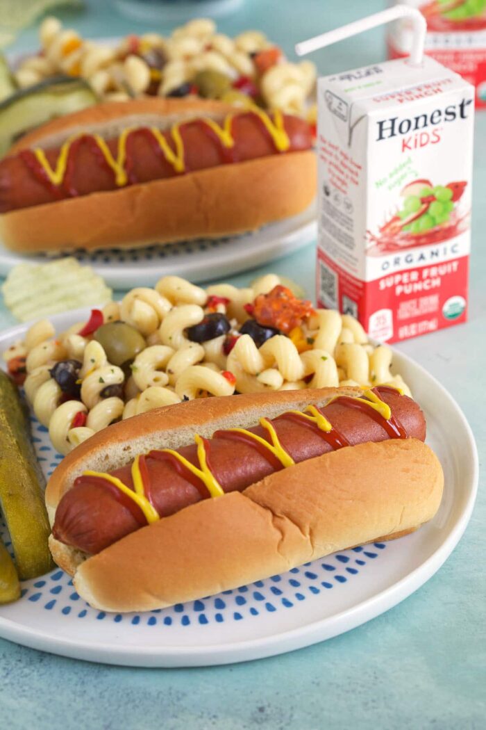 A hot dog is placed next to pickle spears and macaroni salad.