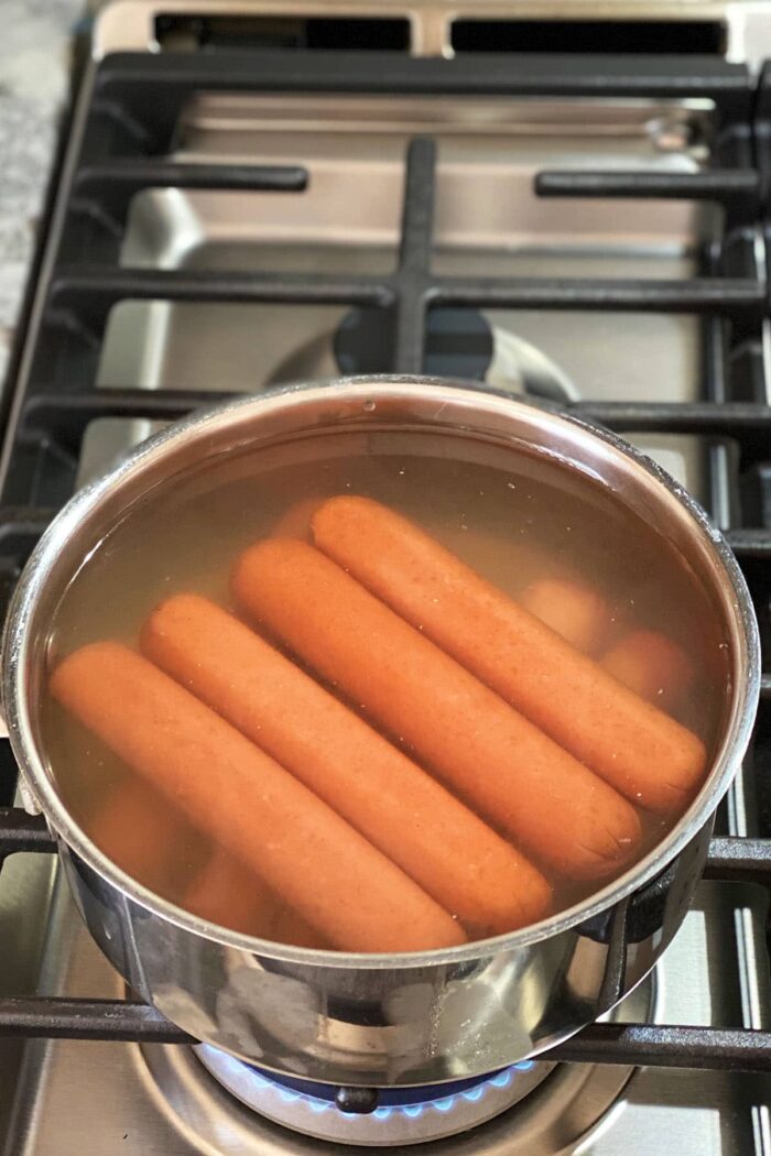 Hot dogs are being boiled on a stovetop. 