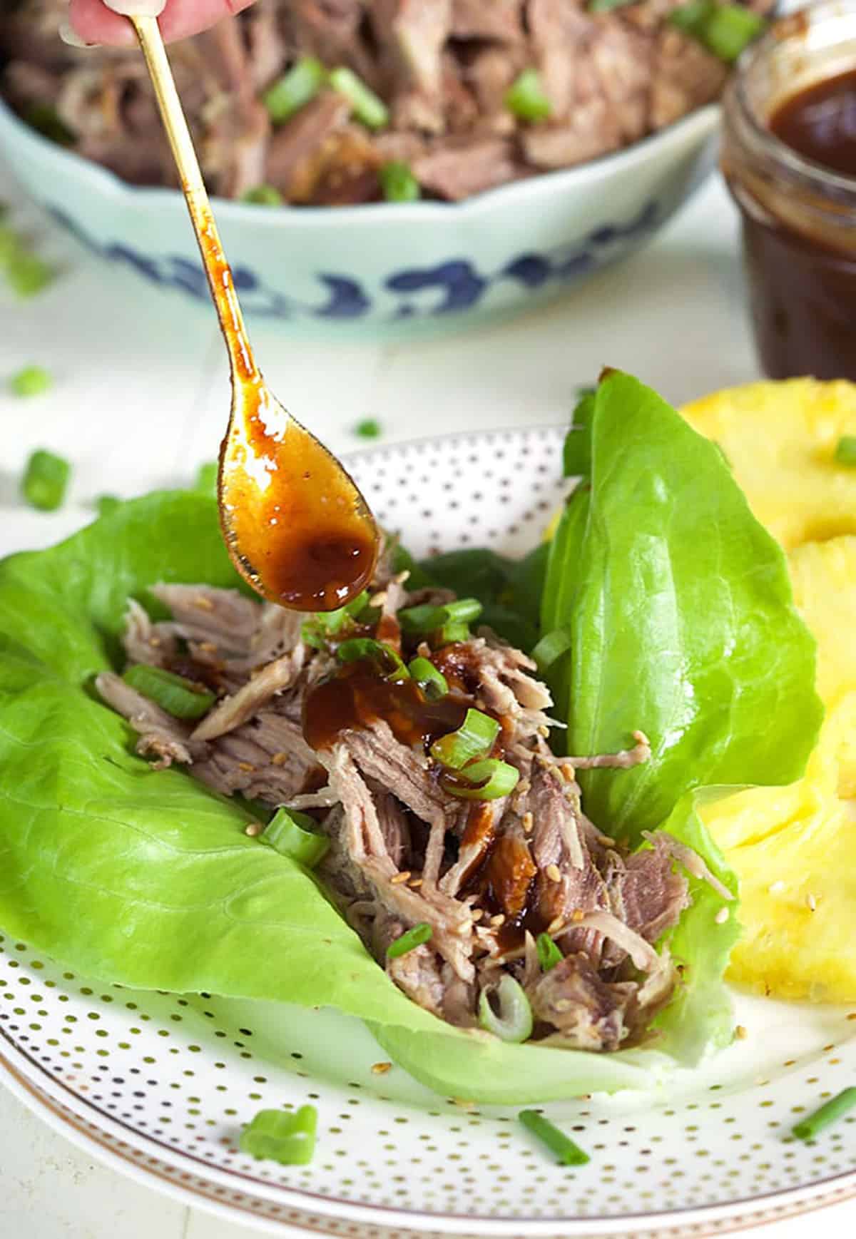 Kalua Pork on a lettuce leaf with a spoon drizzling sauce on top.