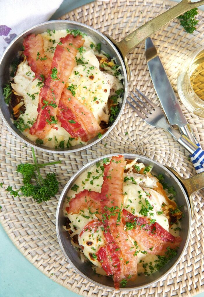 Two Kentucky hot brown sandwiches in mini skillets on a white wicker placemat.