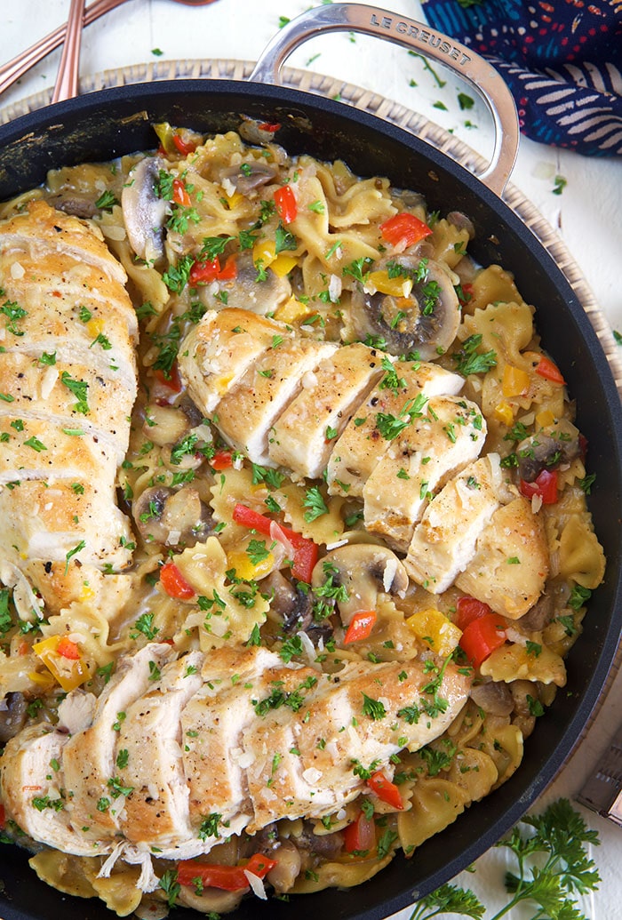 Three sliced chicken breasts are in a skillet filled with cheesy pasta. 