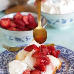 A spoon is drizzling macerated strawberries over a piece of cake.