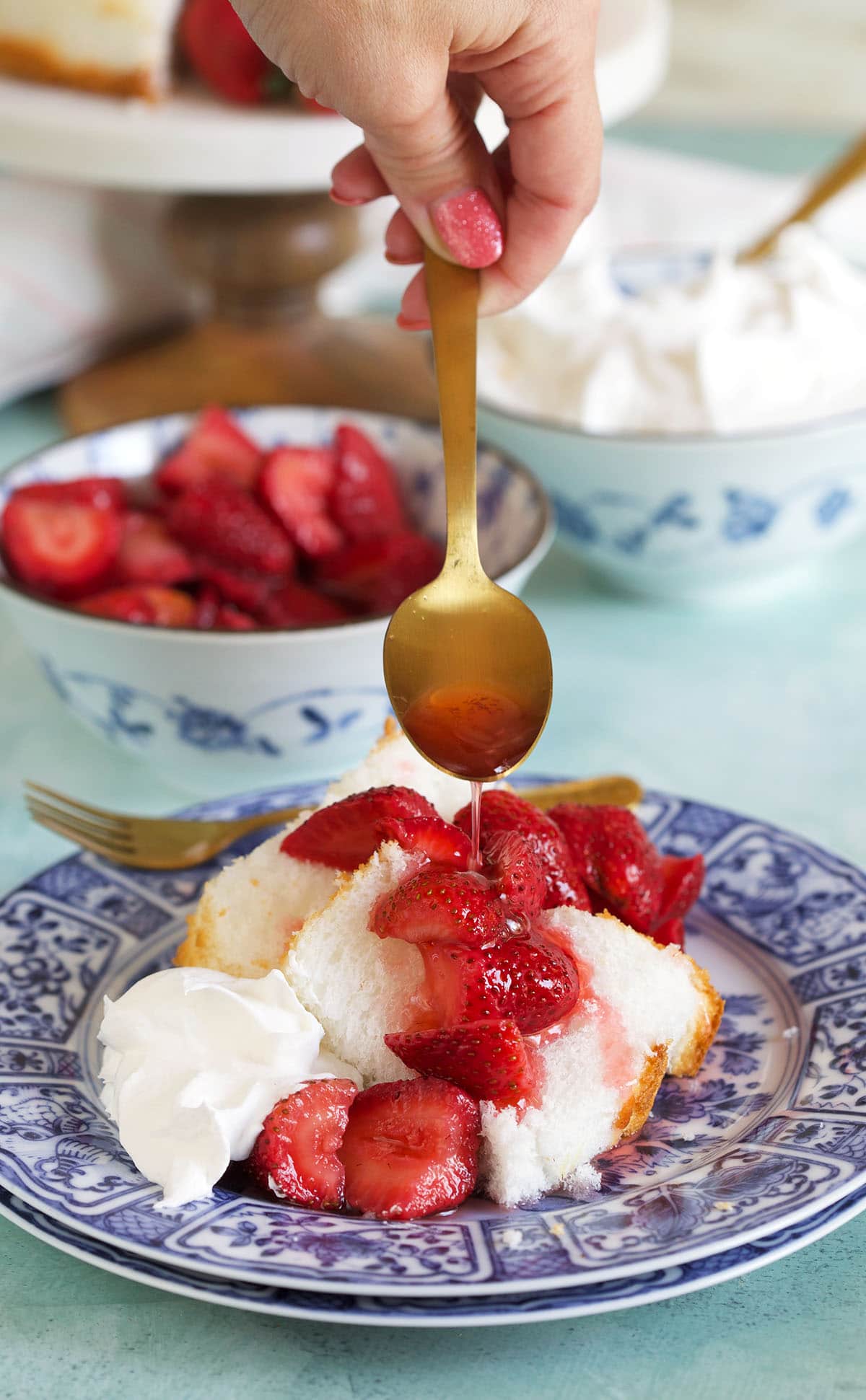 A spoon is drizzling macerated strawberries over a piece of cake. 