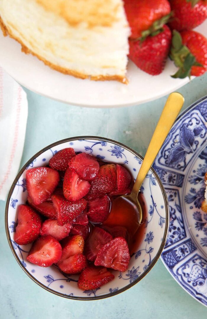A bowl os strawberries is placed next to an angel food cake. 