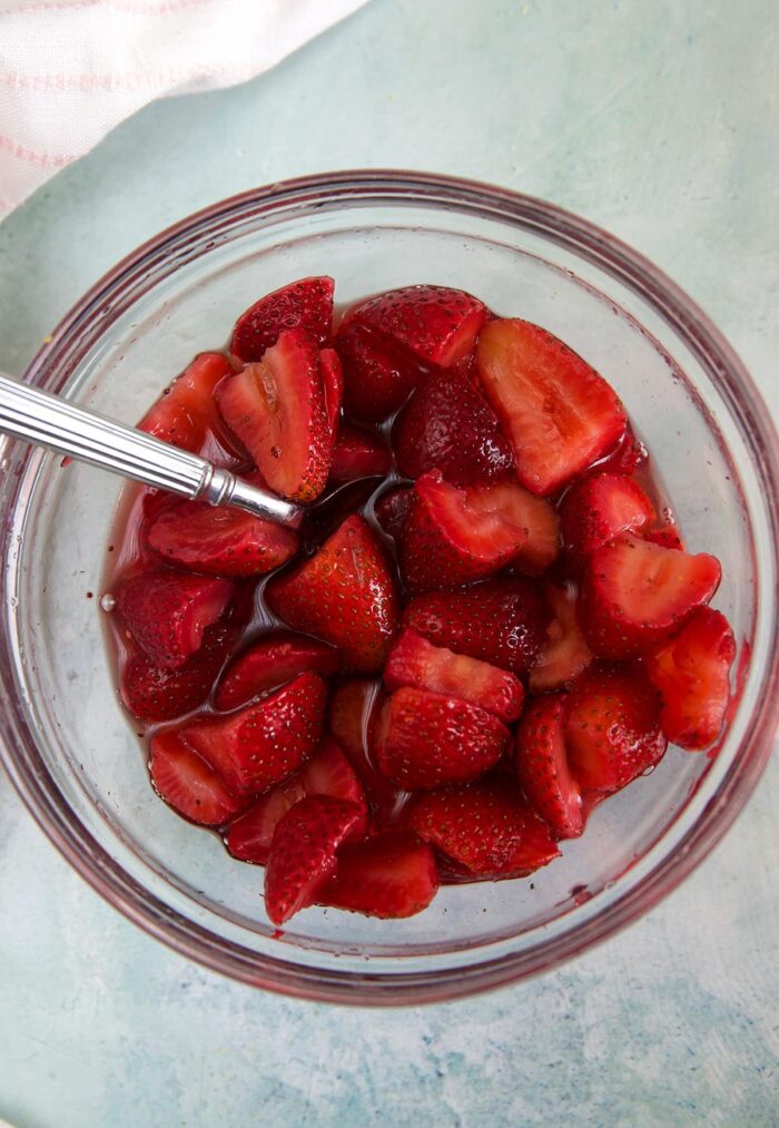 A large glass bowl is filled with juicy macerated strawberries. 