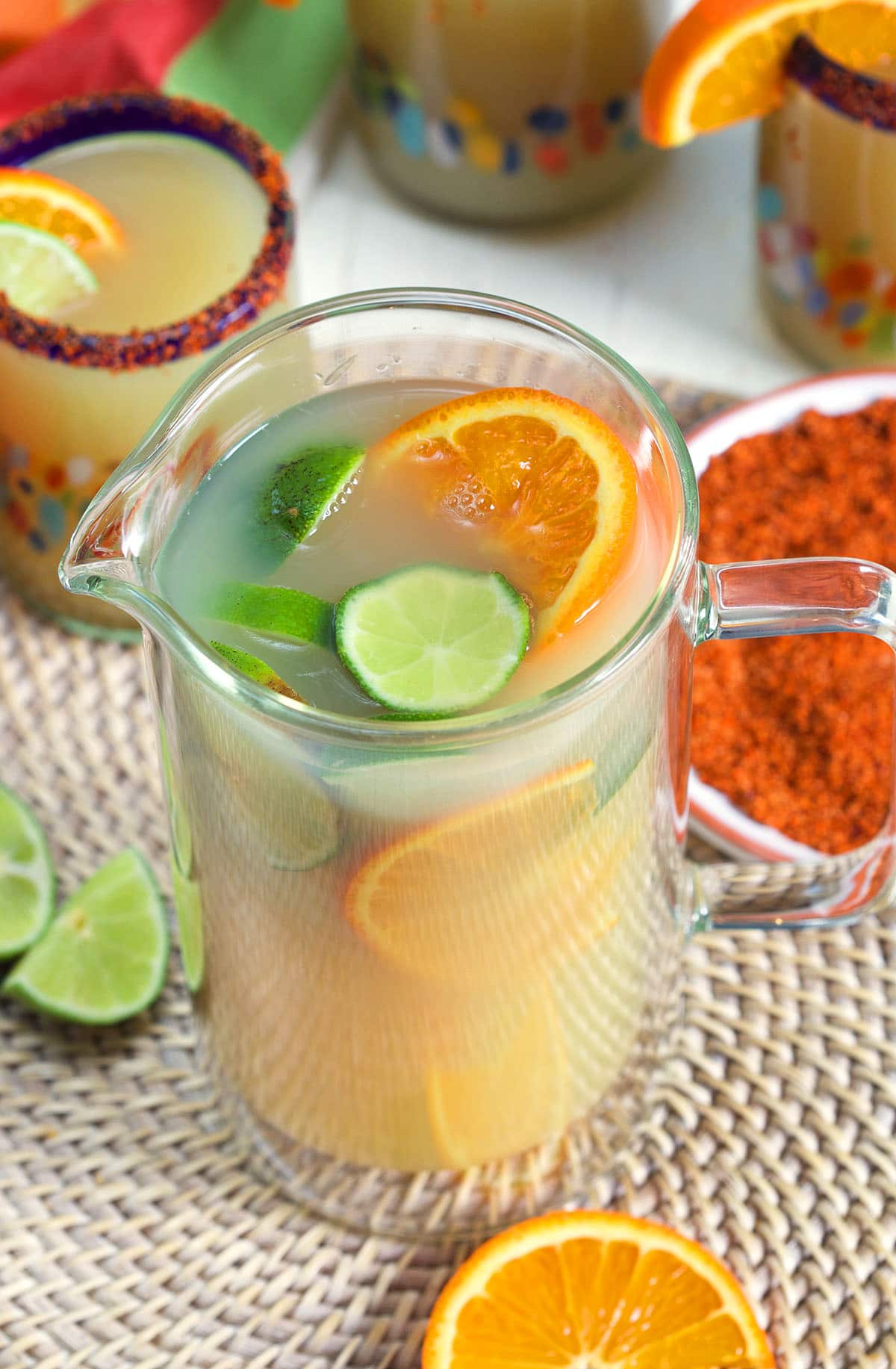 A glass pitched is filled with orange slices, lime slices, and margarita mix. 