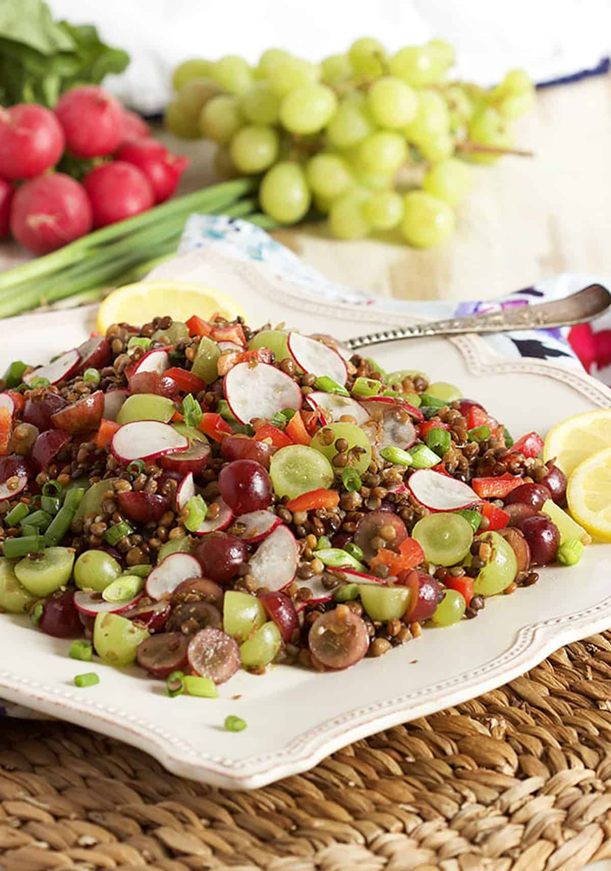 Lentil salad with grapes and radishes on a square platter with a bunch of grapes in the background.