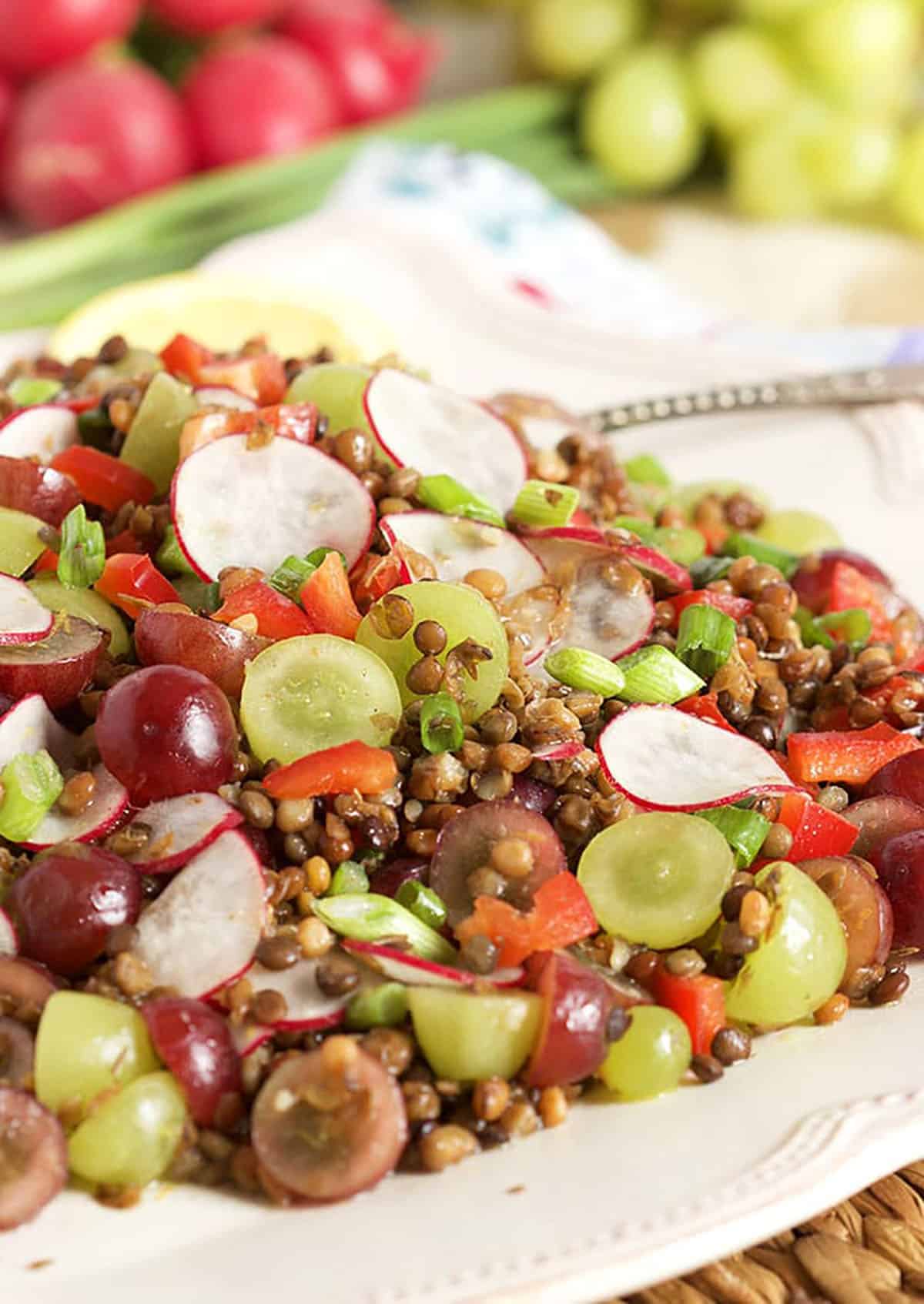 Lentil Salad with grapes and radishes on a white platter with a silver serving spoon.