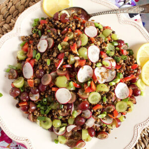 Lentil Salad on a square platter with lemon slices and a silver serving spoon.