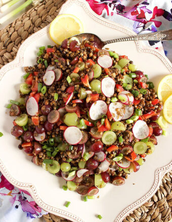 Lentil Salad on a square platter with lemon slices and a silver serving spoon.