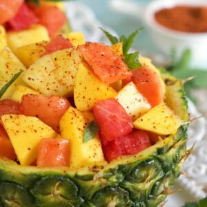 Powder is placed on top of fresh fruit in a pineapple bowl.