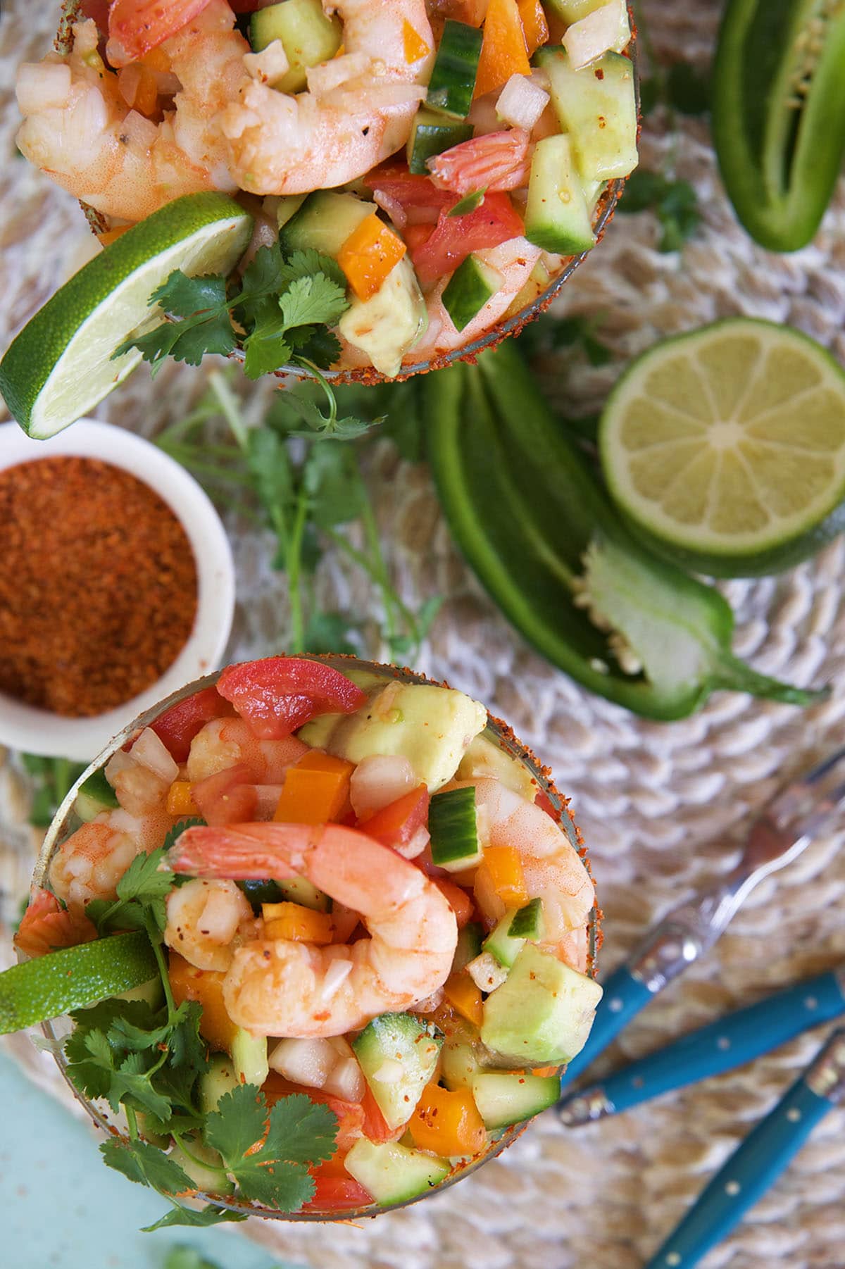 Fresh ingredients like limes and peppers are placed on a surface near Mexican shrimp cocktails. 