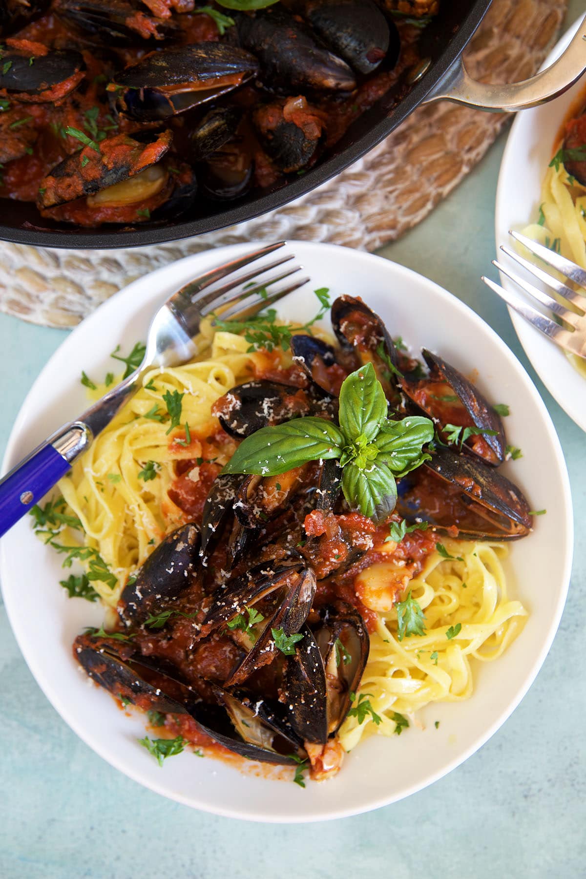 A fork is placed on a white plate filled with mussels and pasta. 