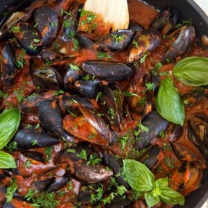 Mussels are being cooked in a large black skillet.