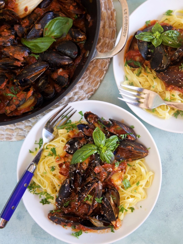 Two plates of mussels marinara are placed next to a skillet.
