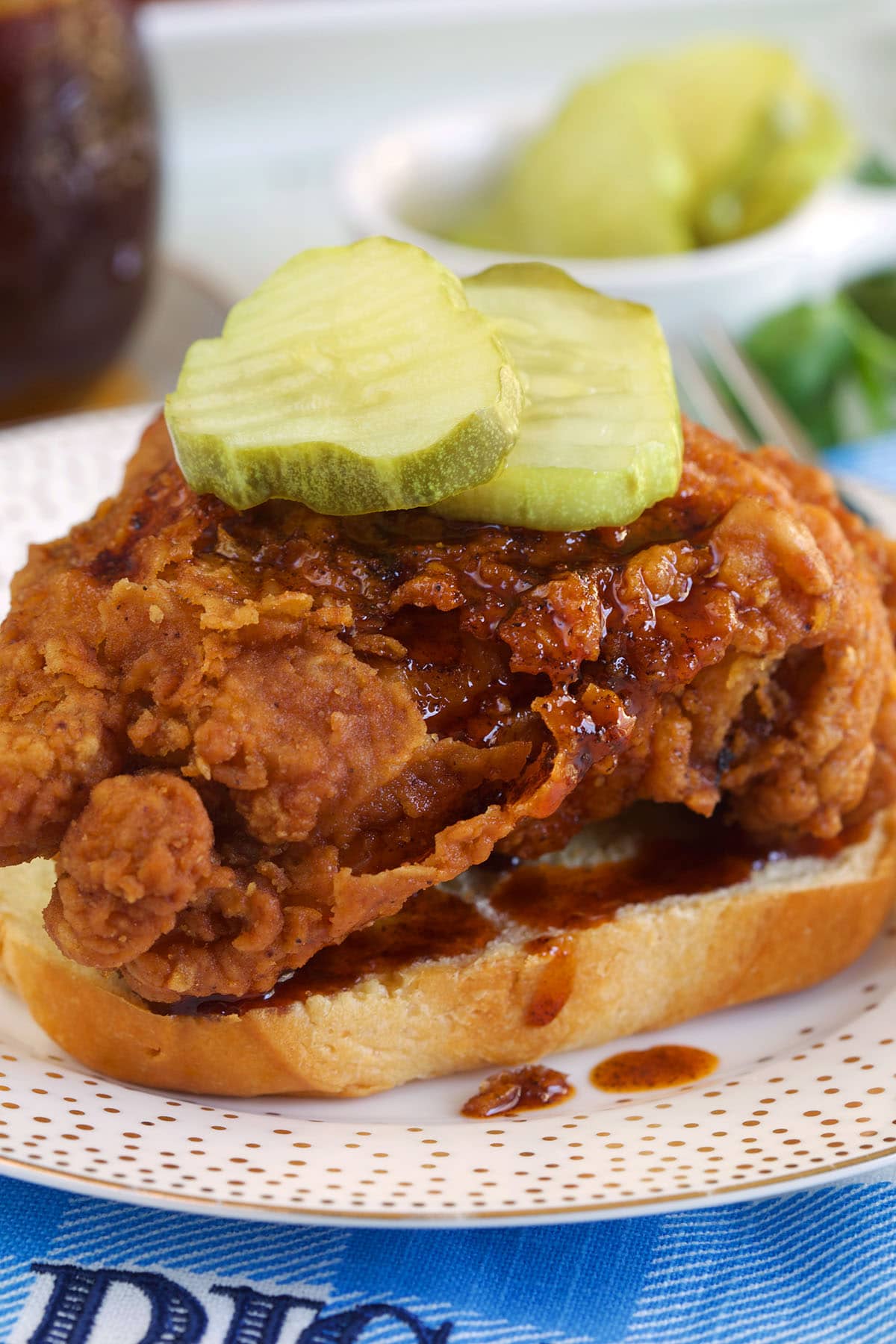 A piece of fried chicken with hot sauce and pickles is on a piece of bread. 