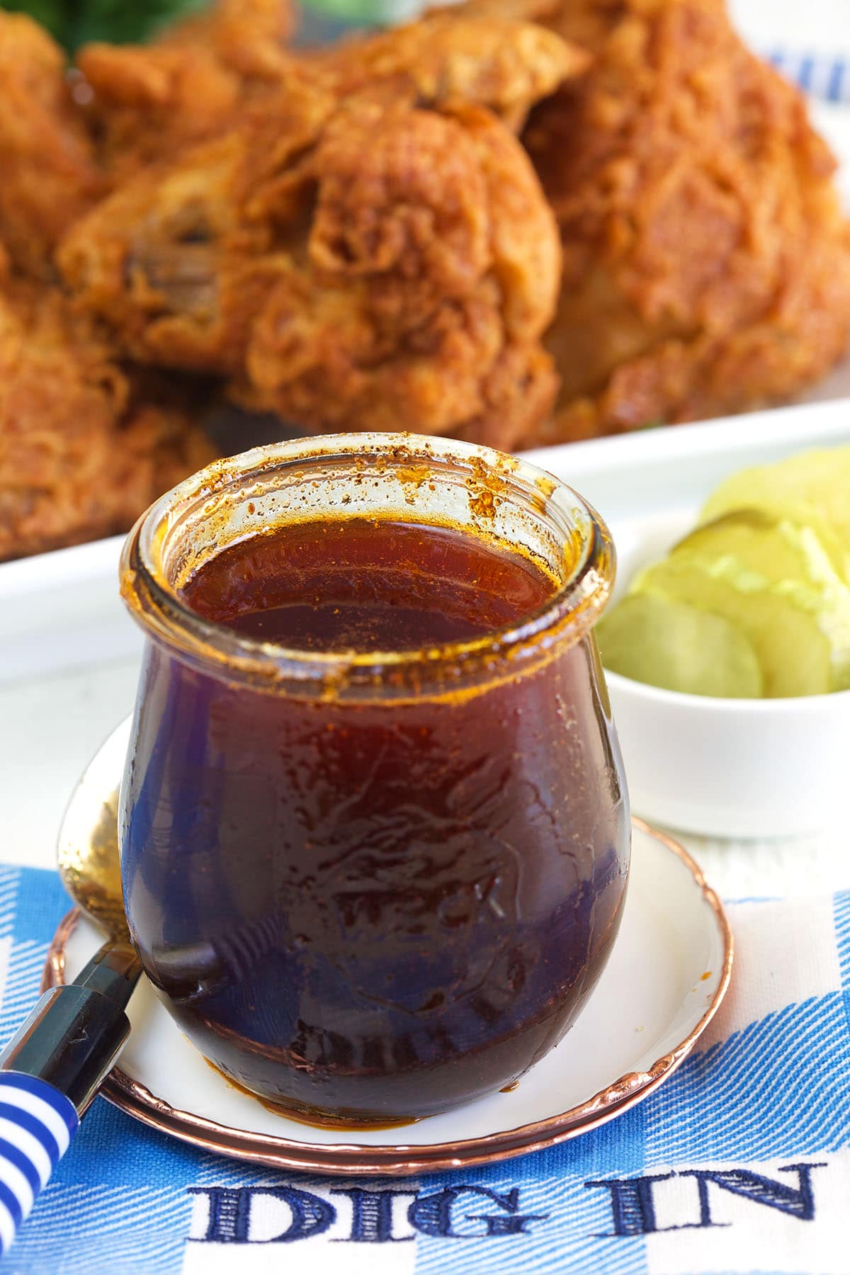 A small jar of hot sauce is placed in front of fried chicken. 