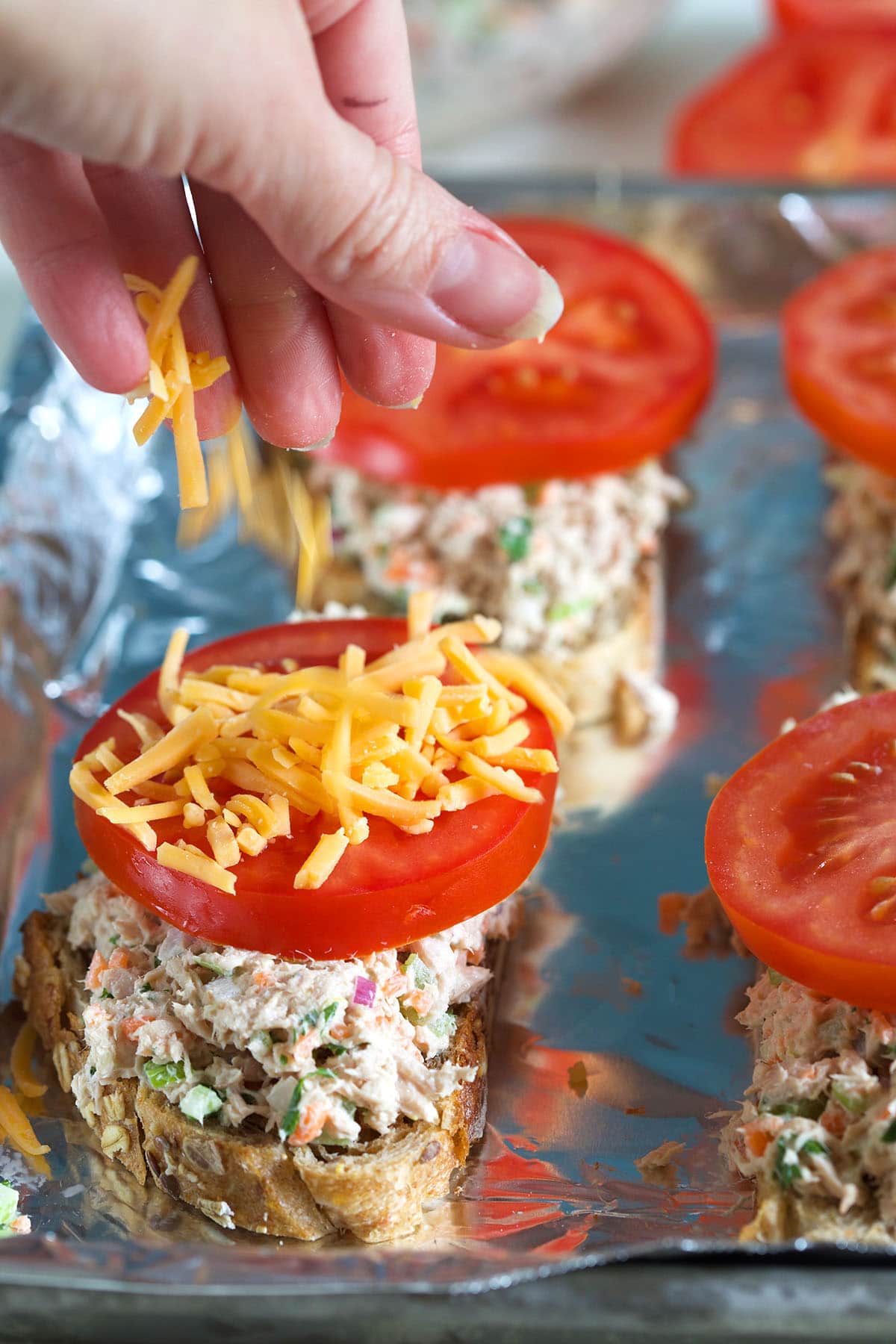 Cheese is being sprinkled onto an un-broiled tuna melt. 