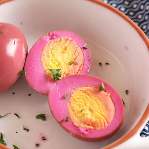 Beet Pickled Egg cut in half on a white dish with parsley sprinkled on it.