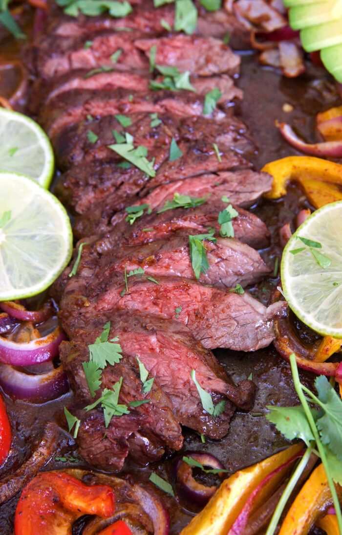 sliced steak on a sheet pan with fajita vegetables.