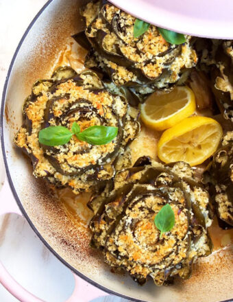 Baked Italian Stuffed Artichokes in a pink dutch oven with lemon slices.