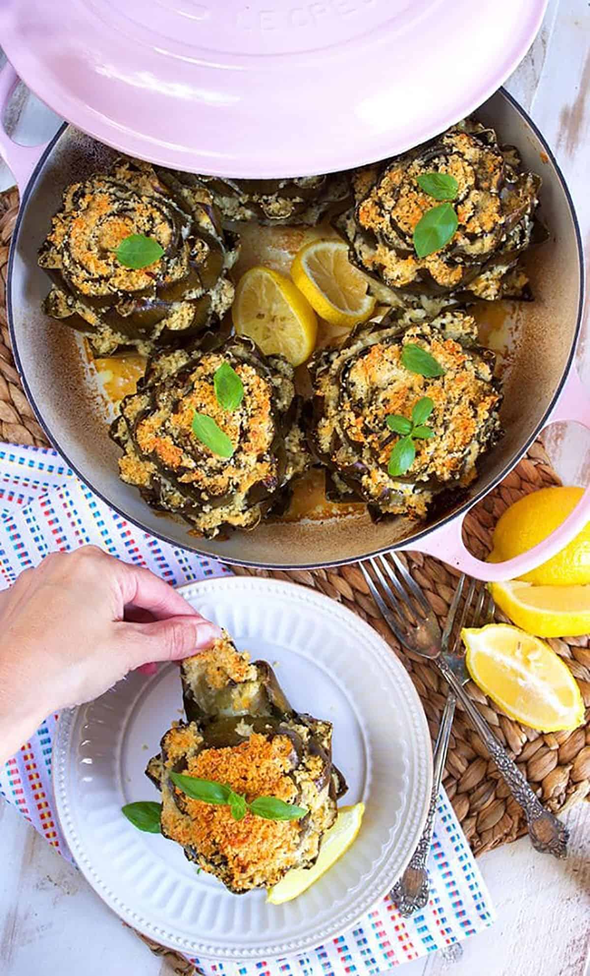 Baked Stuffed Artichokes in a dutch oven with one on a plate.