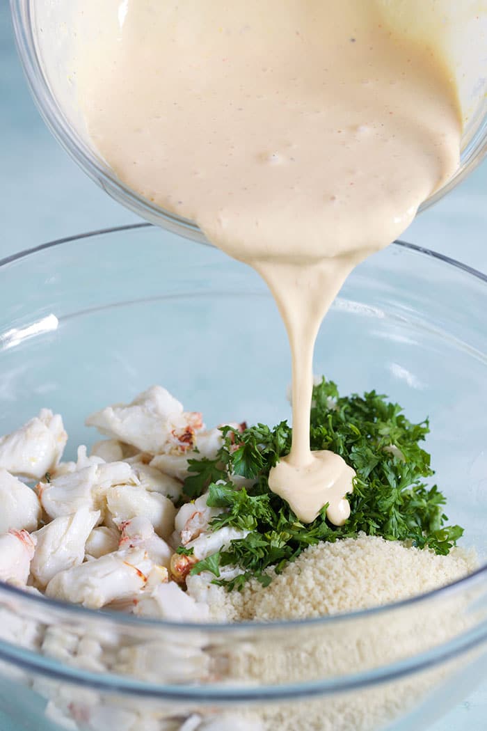 A white sauce is being poured over a glass bowl of ingredients.