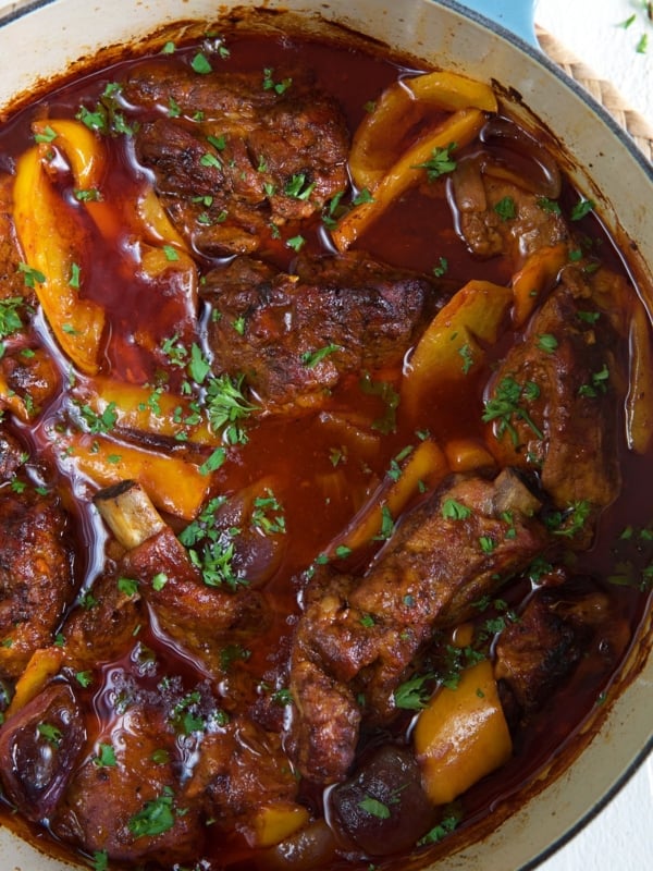 A pot is filled with ribs, peppers and sauce.