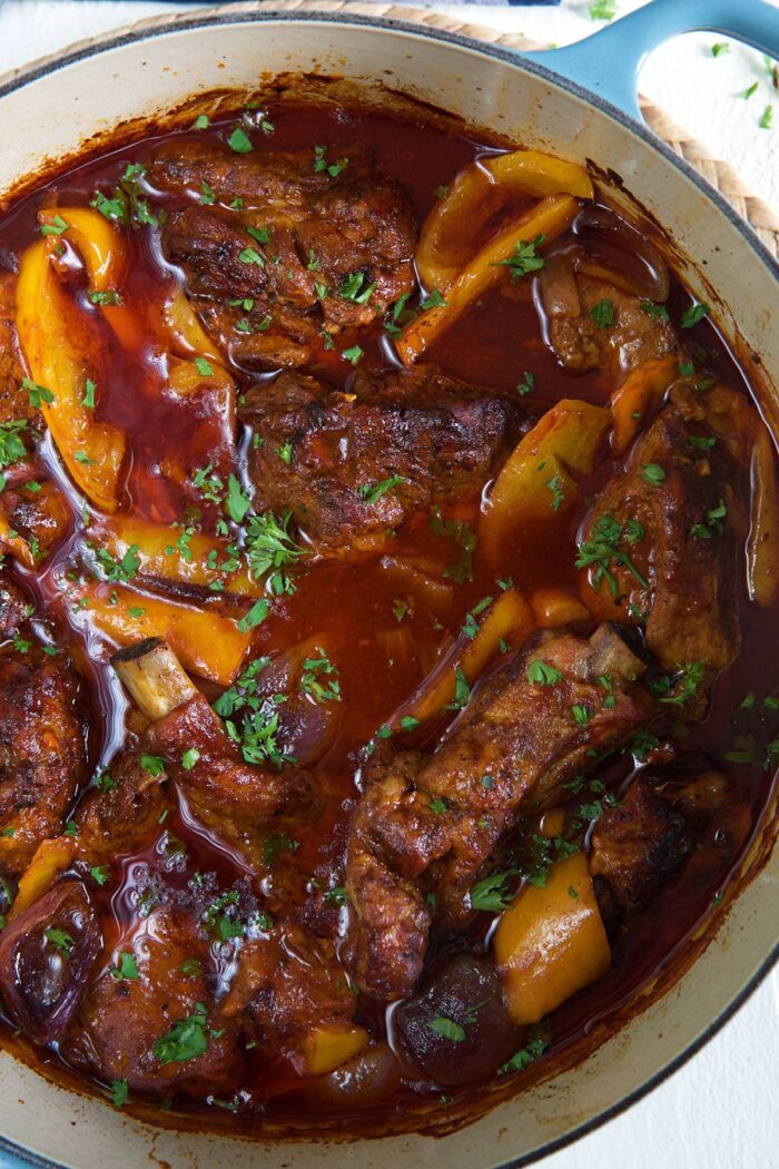 A pot is filled with ribs, peppers and sauce. 