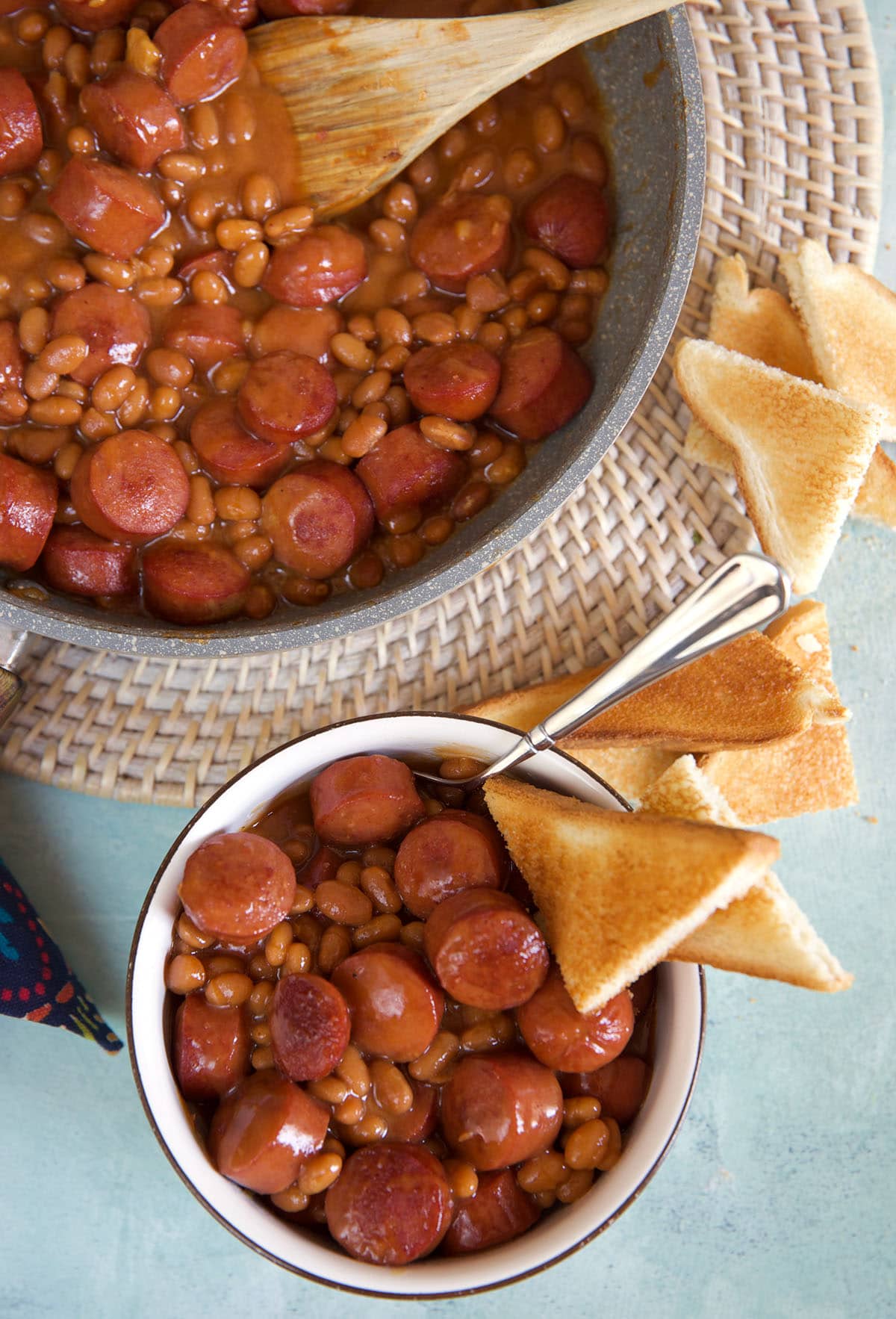 A piece of toast is in a small bowl filled with beans next to a large pot.