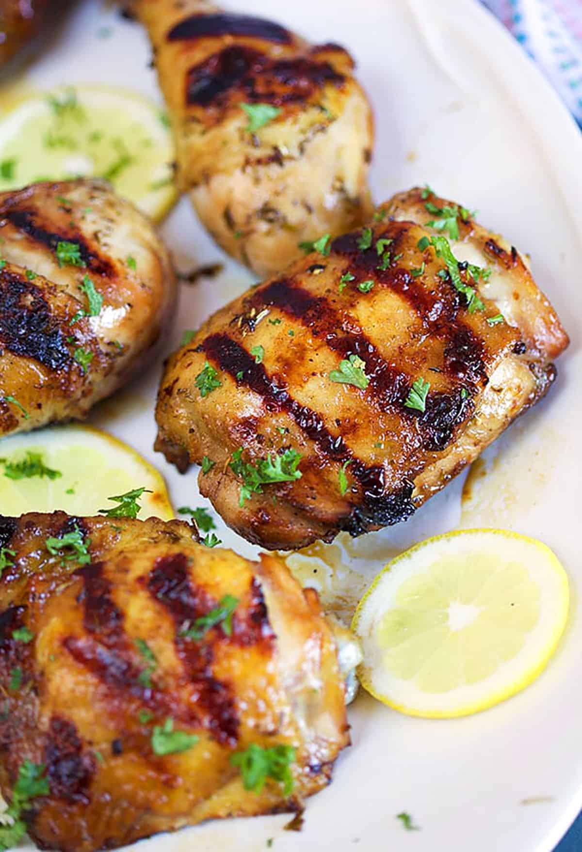 Grilled chicken thighs on a white platter with lemon slices