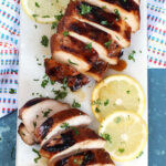 Grilled Marinated Chicken Breasts on a white platter with a blue background.
