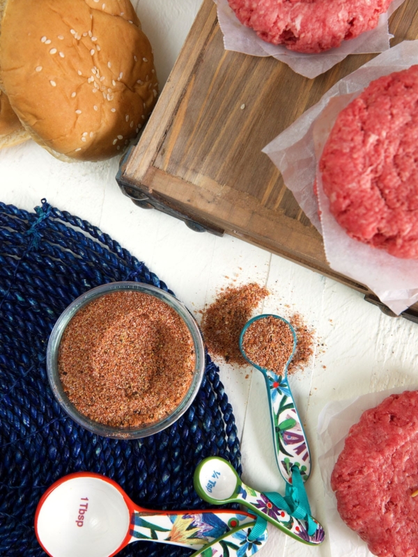 Seasoning is placed next to uncooked burger patties.