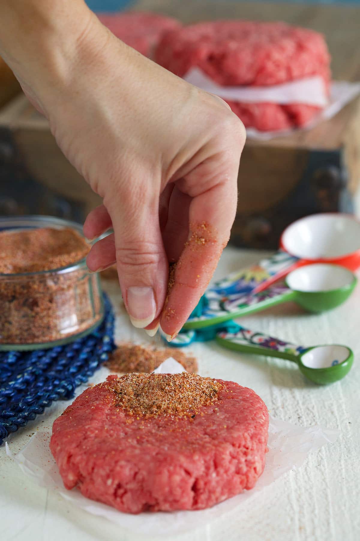 Seasoning is being sprinkled on top of a hamburger patty.