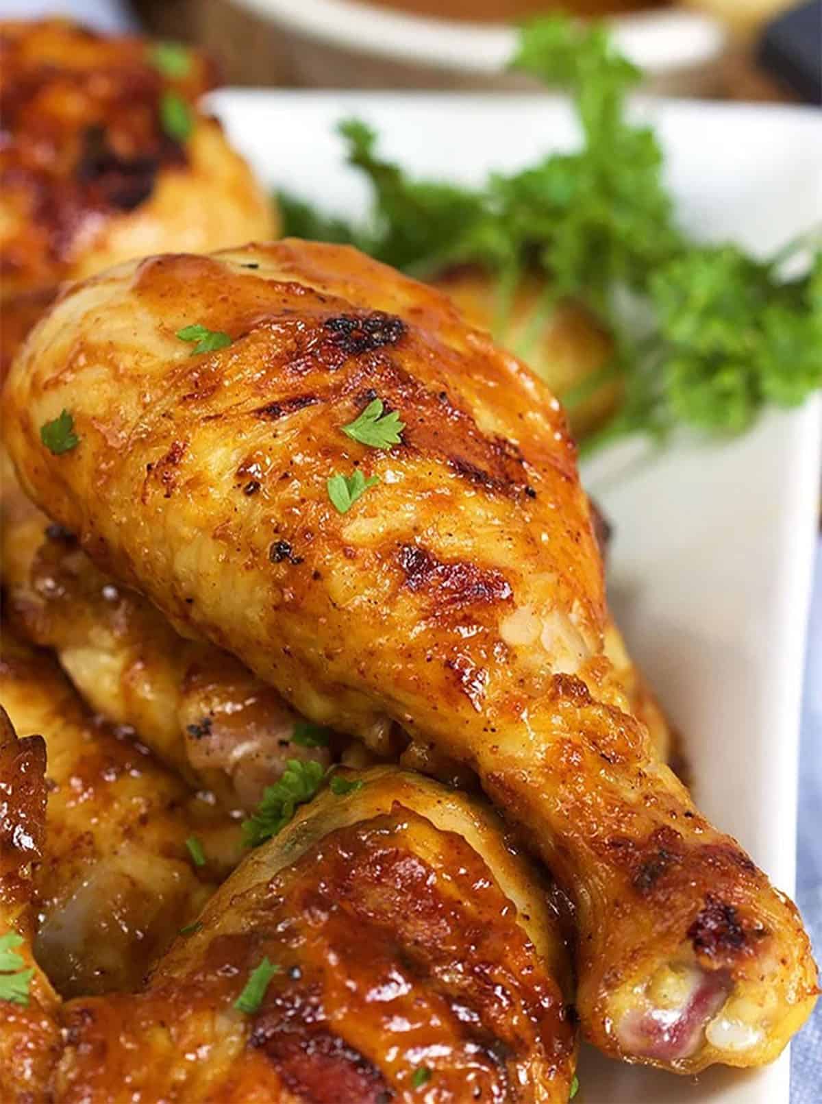 a bbq chicken drumstick on a white platter with a sprig of parsley.