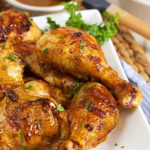 Carolina Gold BBQ Chicken on a white platter with a bowl of Carolina Gold bbq sauce in the background.